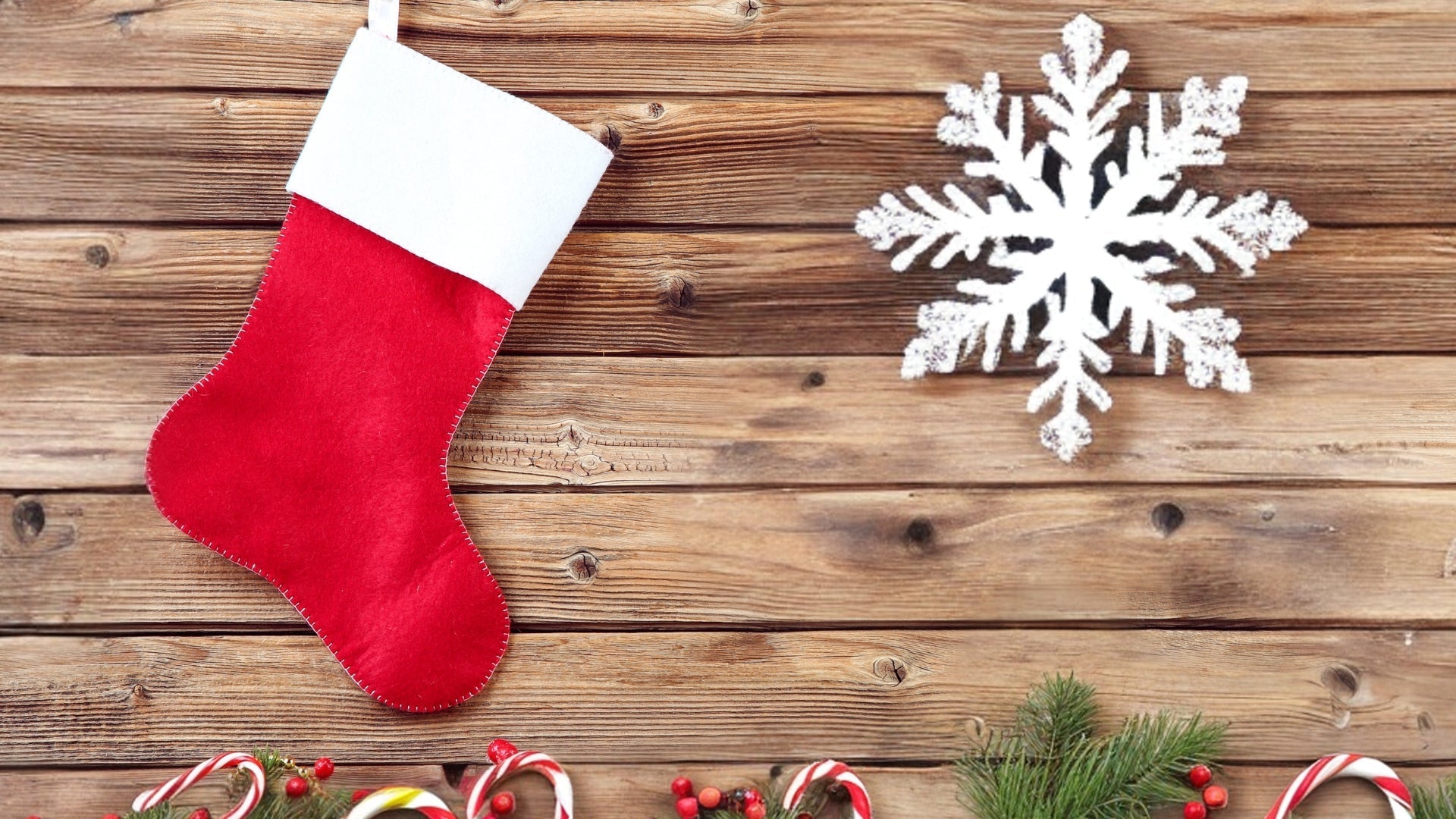 Red Christmas stocking hanging with natural wood panel background, red and white candy canes, small pinecones and sprigs of green Christmas foliage