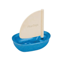 A small toy sailboat with a blue base and a beige sail, made from PlanWood and natural rubber, with the PlanToys logo visible on the sail.