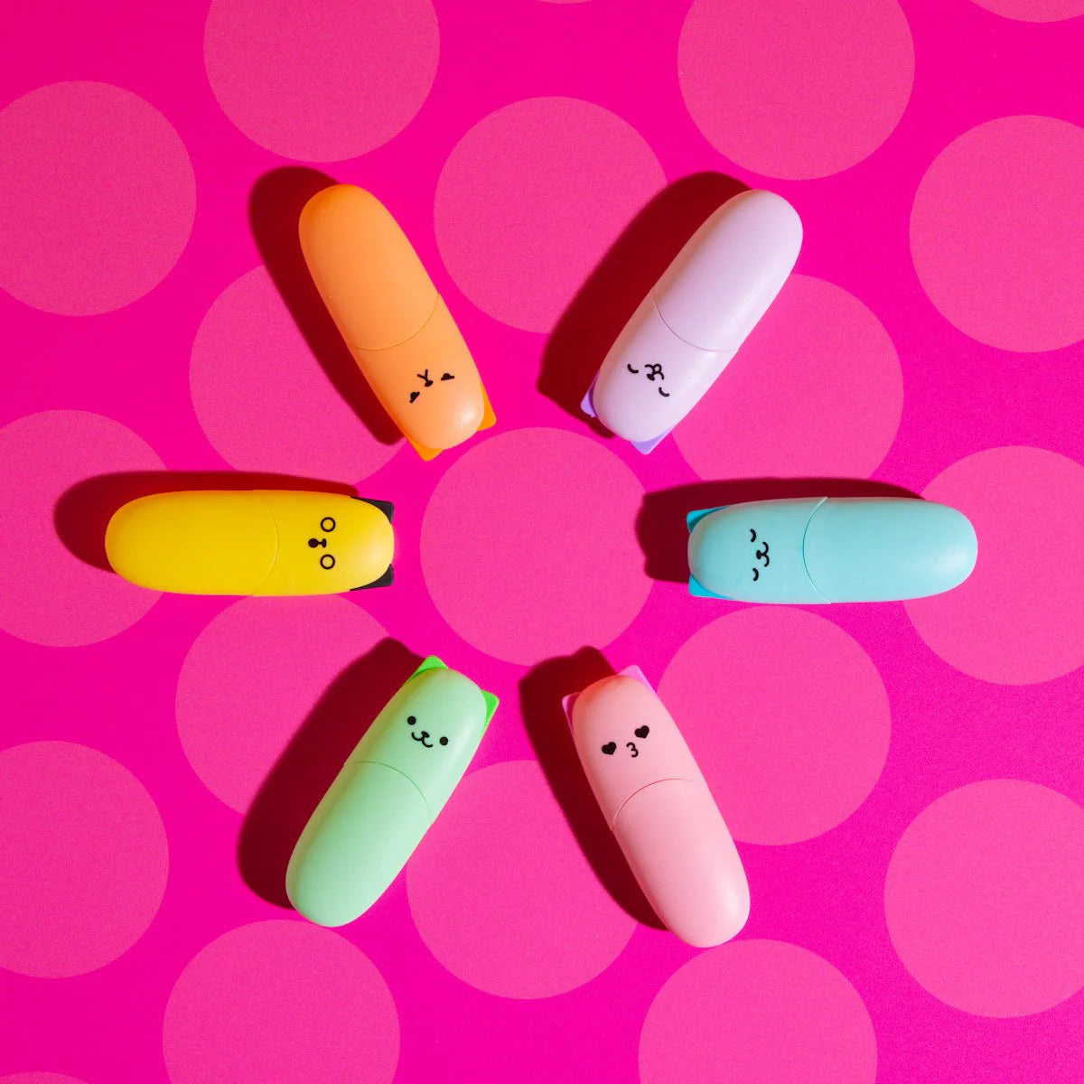 Colorful highlighters with smiley faces on a pink polka dot background