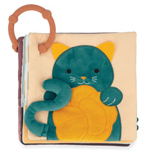 A soft sensory book with a green embroidered patch of a cat on one side, and a brown ring for hanging. The book is made of fabric with different textures and colors.