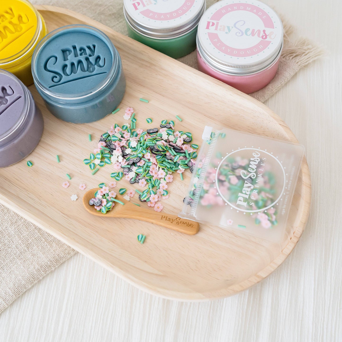 A variety of colorful sprinkles with butterfly designs spread out on a wooden tray, with containers labeled 'Play Sense' in the background.
