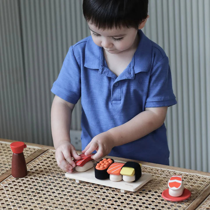 Child playing with toy sushi set on a wooden table