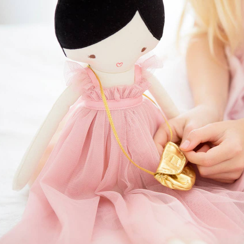 Child holding a gold shaped object next to a doll in a pink dress on a white background
