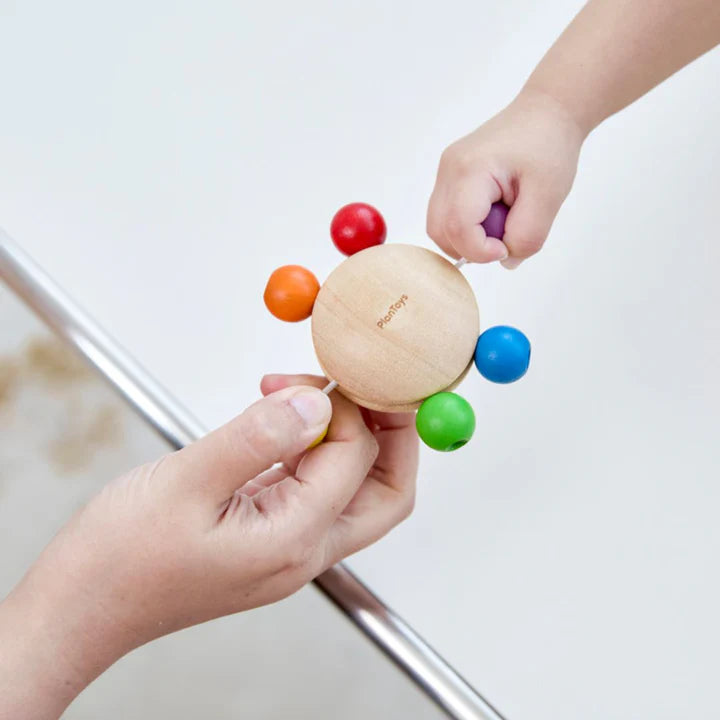 Child's hand holding a wooden rattle with colorful beads on a light background