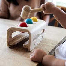 Child playing with a wooden toy hammer and colorful targets on a table.
