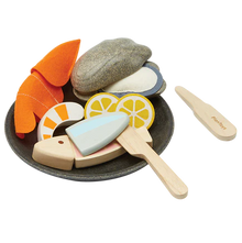 Wooden toy set resembling a seafood platter with pieces of fish, shrimp, oyster, and lemon slices, along with utensils and a plate.