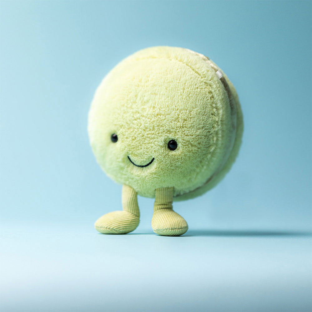Plush toy resembling a pistachio macaroon with a smiling face on a light blue background