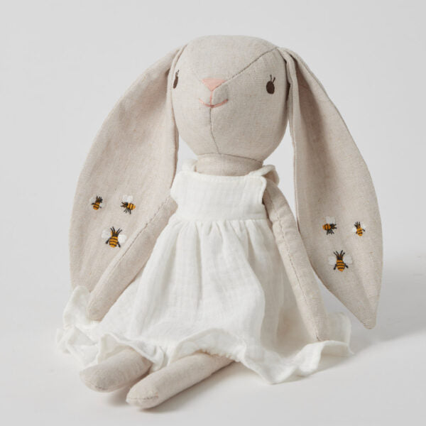 Stuffed toy in the shape of a bunny with a white floral dress and embroidered details, including bees on the skirt.