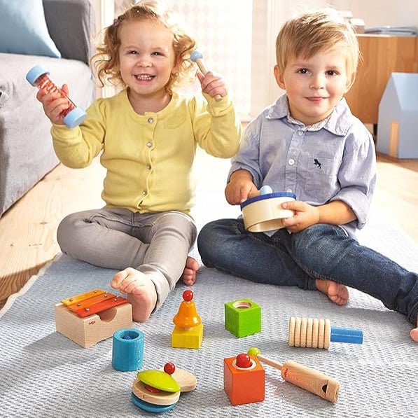 Two children playing with a 12-piece music maker set by HABA, including various musical instruments and sound effect toys.