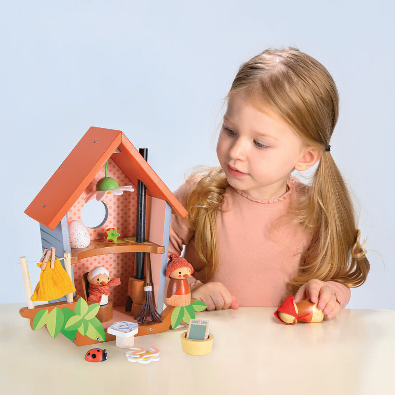 Young girl playing with a wooden dollhouse and accessories on a light blue background