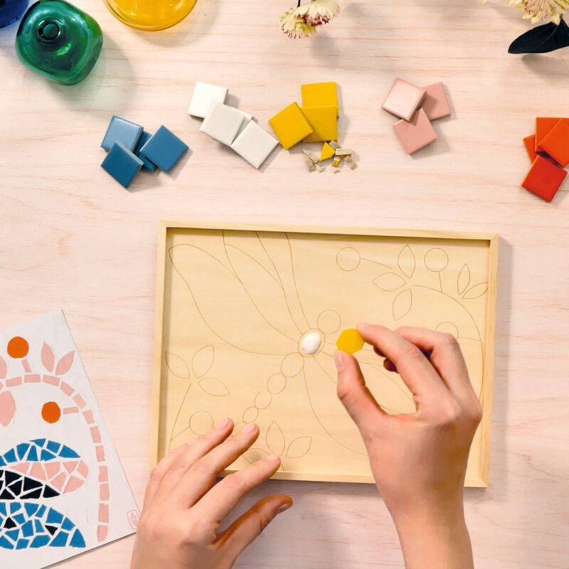 Person assembling a wooden puzzle with colorful pieces on a light surface.