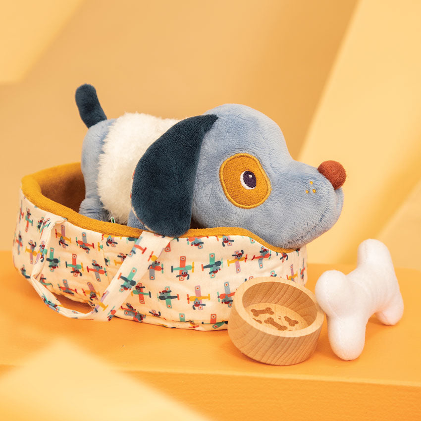 Plush dog toy with a patterned bed, wooden bowl, and white bone on an orange background