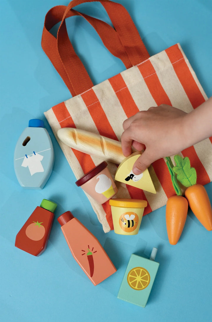 Colorful wooden toys on a striped bag with a hand reaching for one of the toys against a blue background.