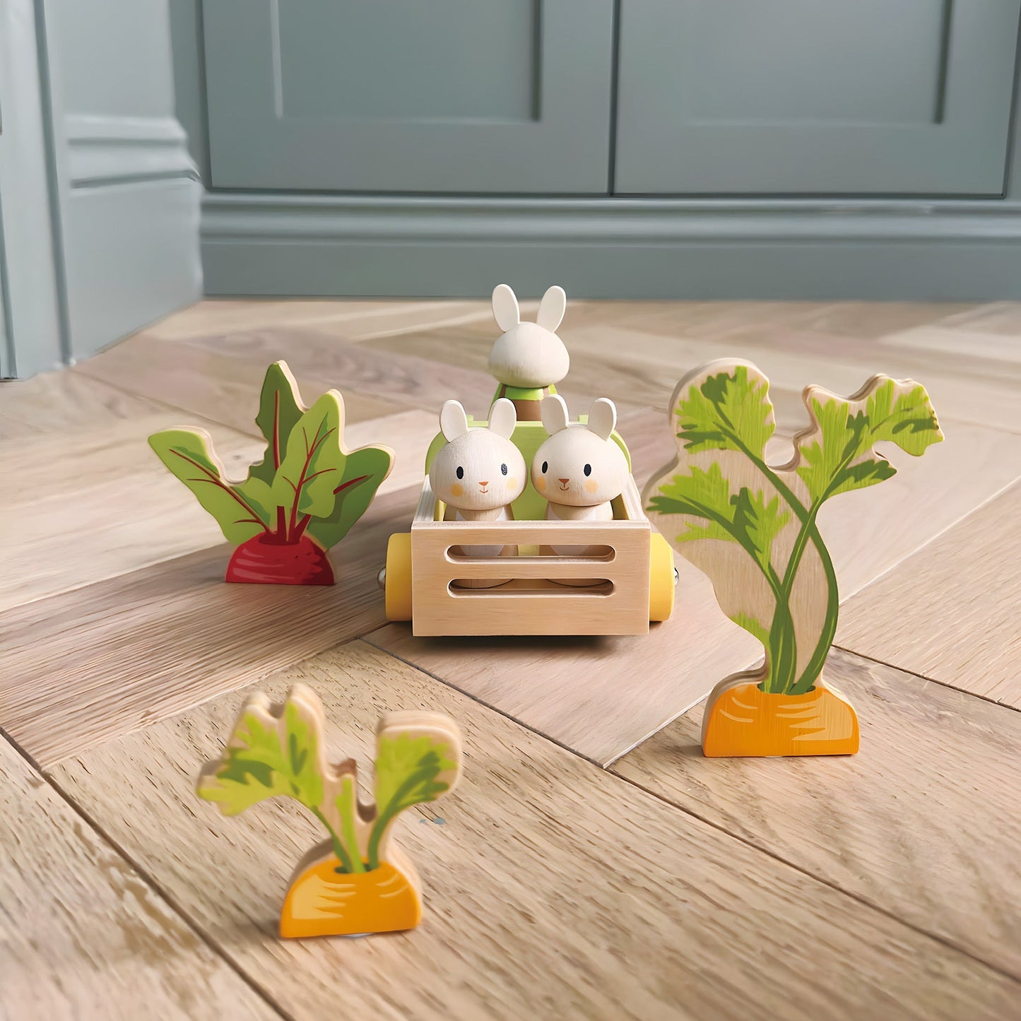 Wooden toy set with rabbits and plants on a wooden floor.