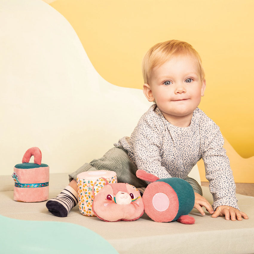 Baby playing with colorful soft toys against a yellow background