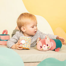 Child playing with a plush toy and a container on a light-colored surface with a yellow background