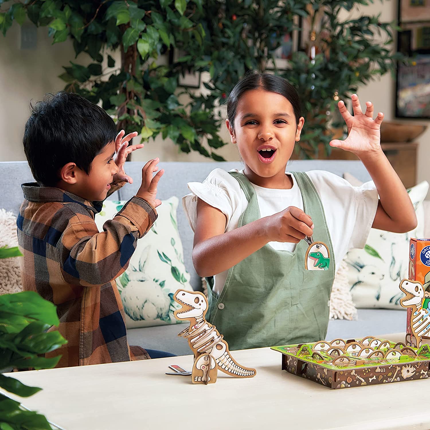 Two children playing with dinosaur toys on a table, surrounded by plants.