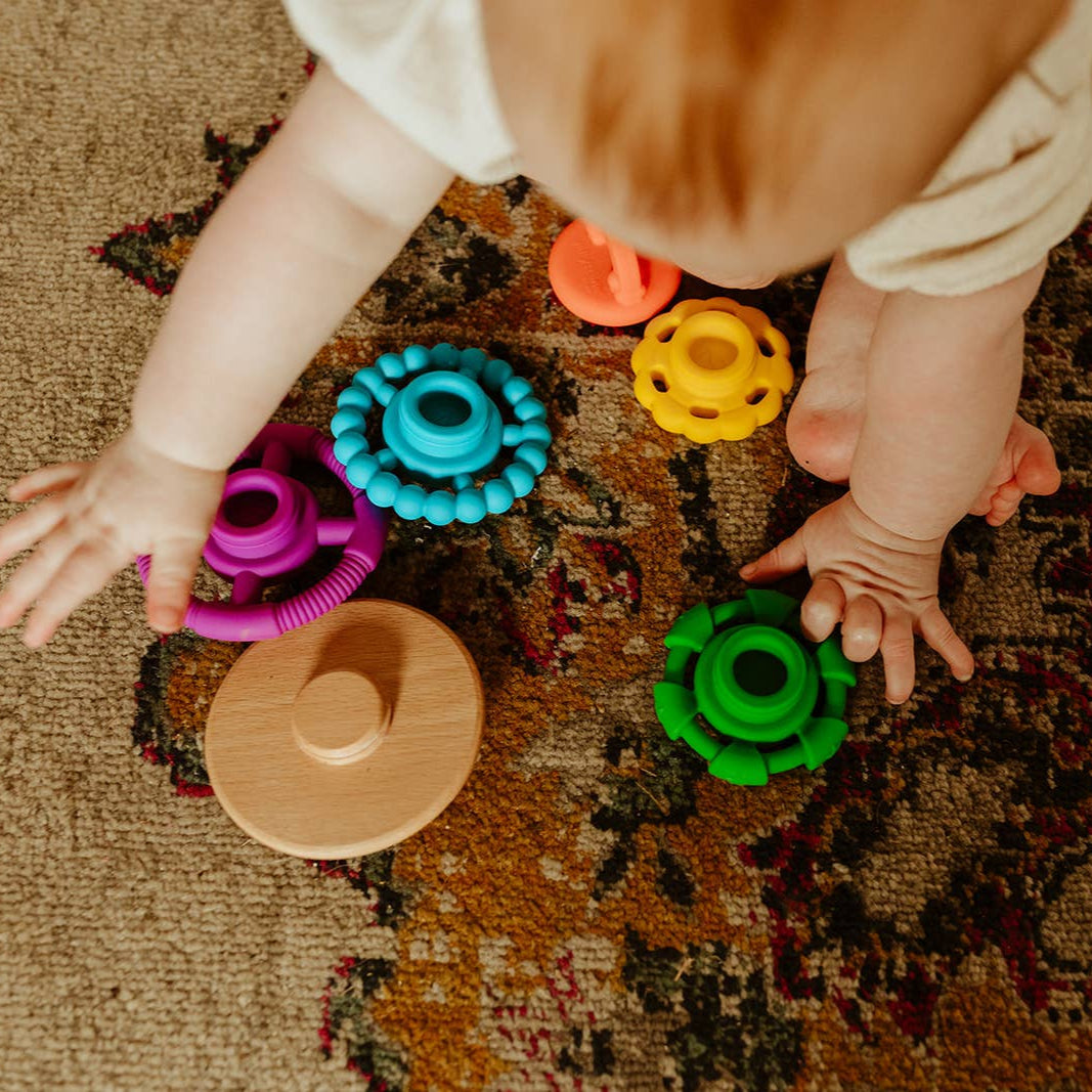 Baby playing with bright rainbow silicone stacking toy with wooden wobble base