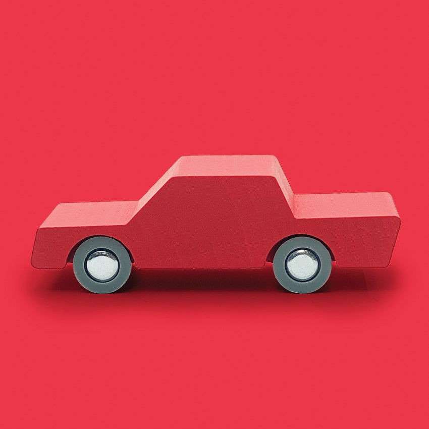 Red wooden toy car with grey wheels, pictured on a bright red background