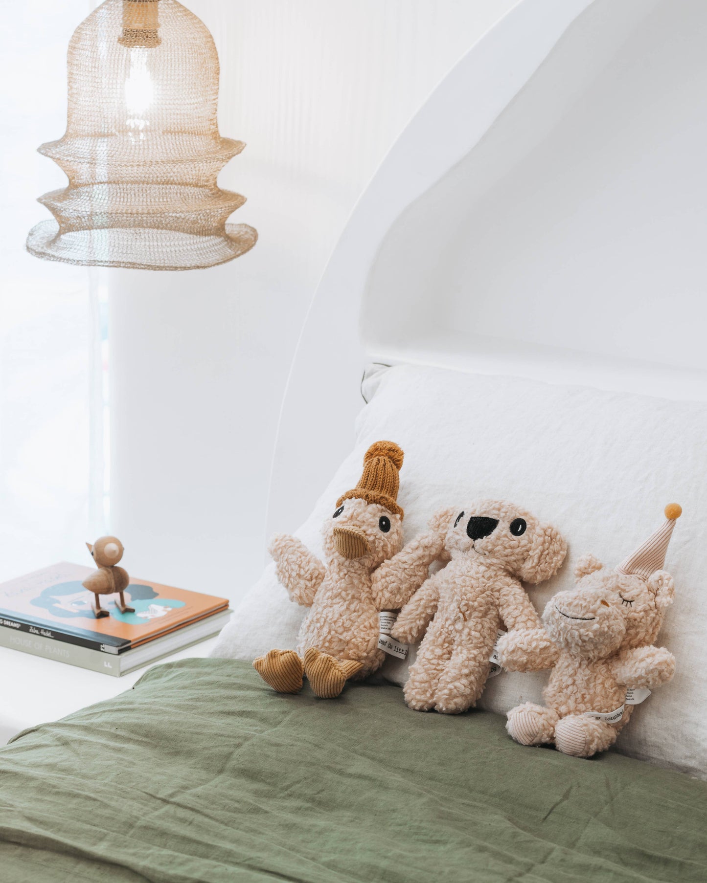 Three plush toys on a bed with a lamp and book in the background