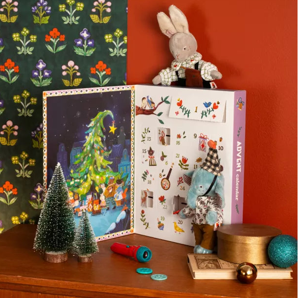 Advent calendar with Christmas-themed illustrations on a wooden surface with decorative items.
