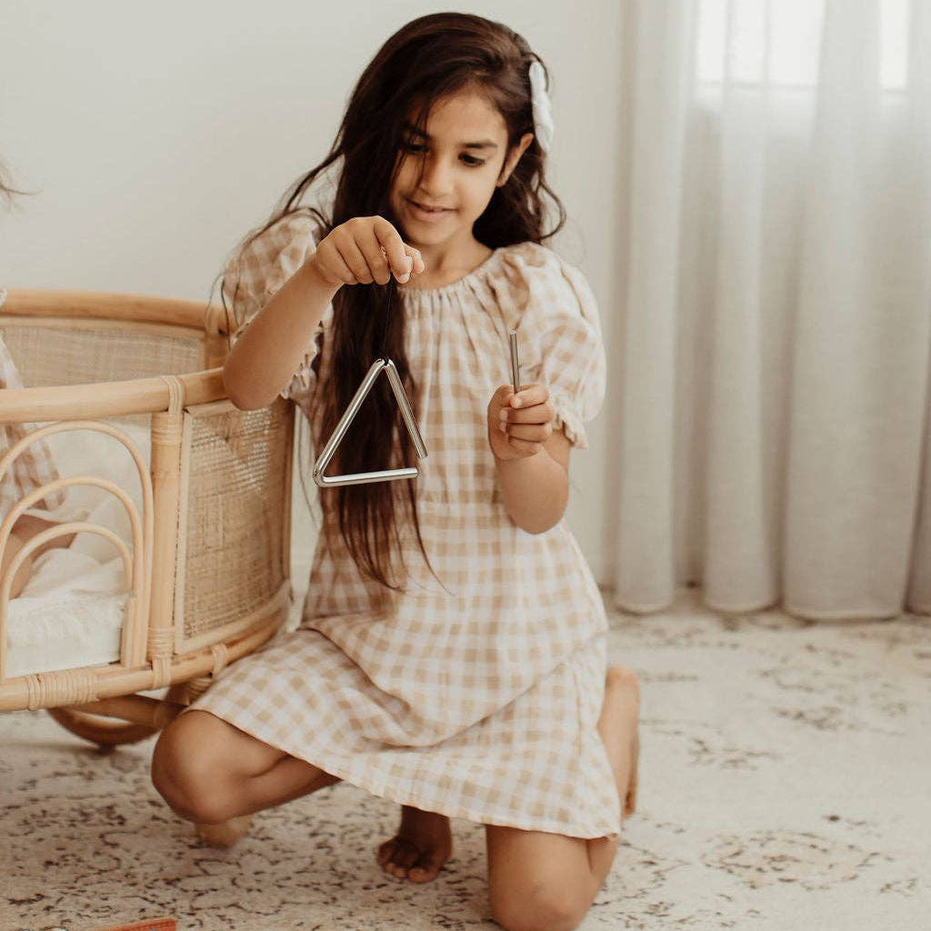 Child in a gingham dress playing the Love Note Co mini triangle in a bright playroom.