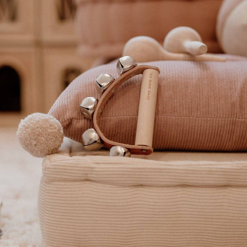 Love Note Co handbells resting on a dusty pink cushion in a warm neutral playroom.