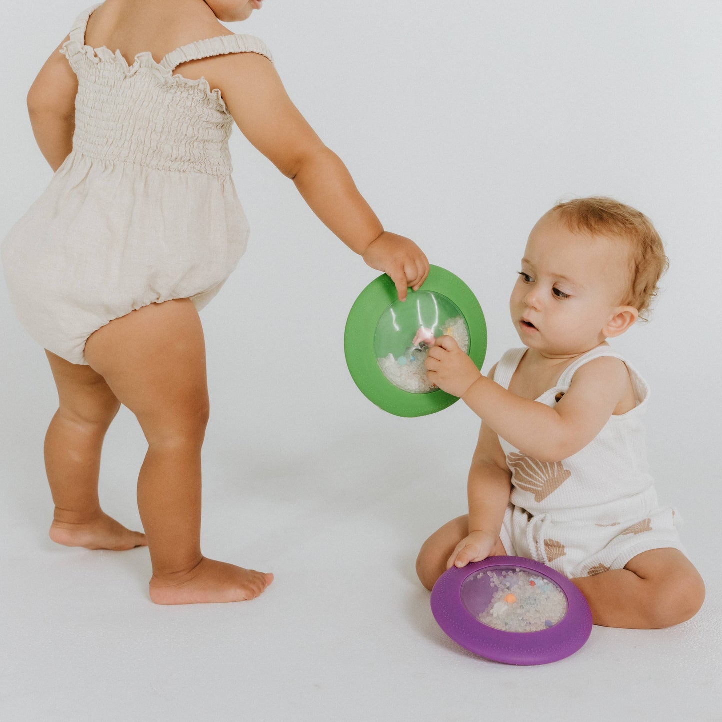 toddlers holding green and purple Jellystone Design silicone peekaboo sensory bags