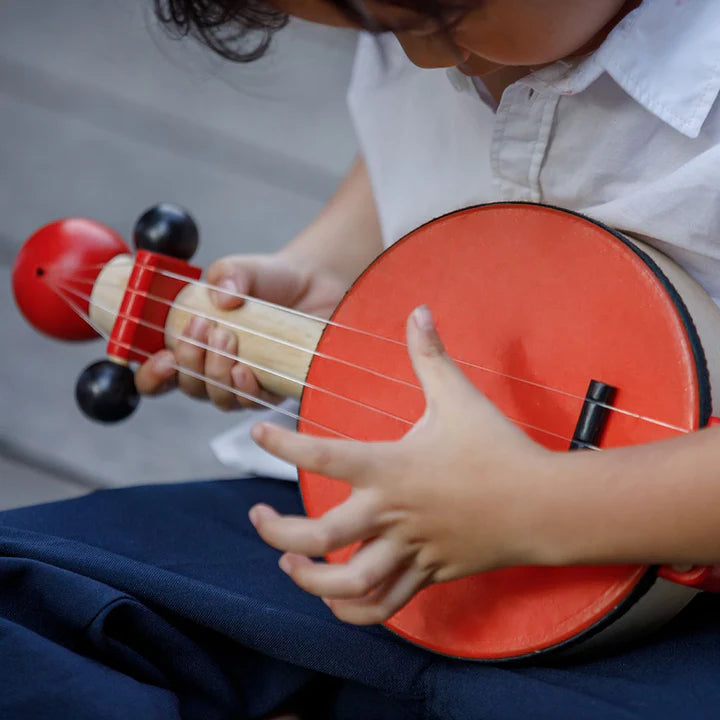 Person playing a red ukulele with a neutral background