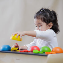 Child playing with colorful  wooden cup 's and matching wooden counting chips on a table.