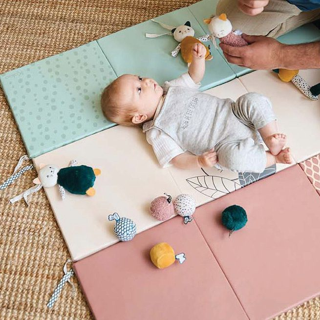 Baby lying on playmat surrounded by soft tactile baby toys