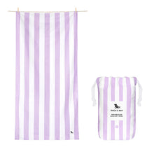 A lilac and white striped beach towel with a brand logo on the bottom corner, displayed on a hanger and next to its packaging.