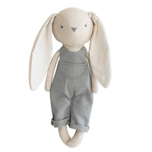 A grey and beige cotton-linen fabric stuffed bunny with embroidered face, dressed in overalls, standing upright.