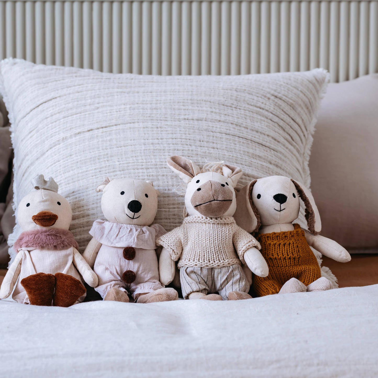 Four plush toys on a bed with a textured pillow in the background