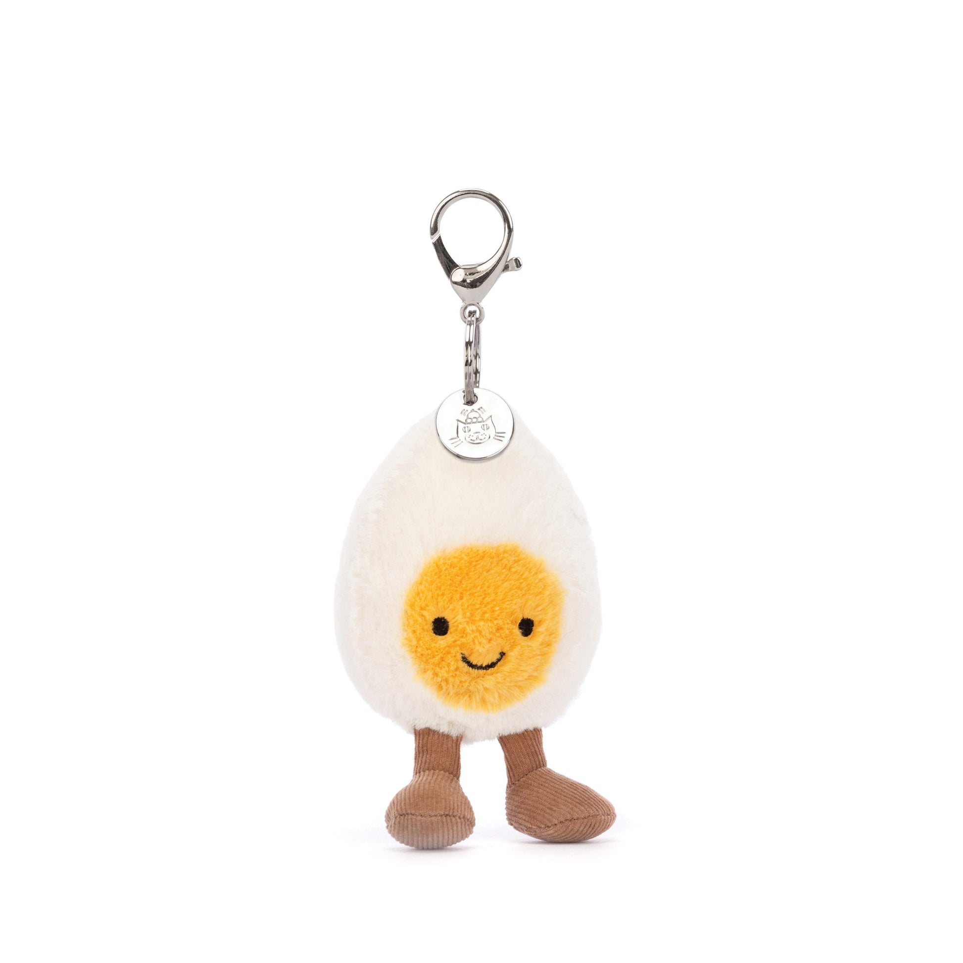 A plush toy resembling a boiled egg with a cream-colored body, yellow yolk, and brown cordy legs, attached to a keyring with a round metal Jellycat logo disc.