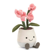 A plush toy representing a pink orchid with pale orange columns in a white pot with a smiling face and brown roots.