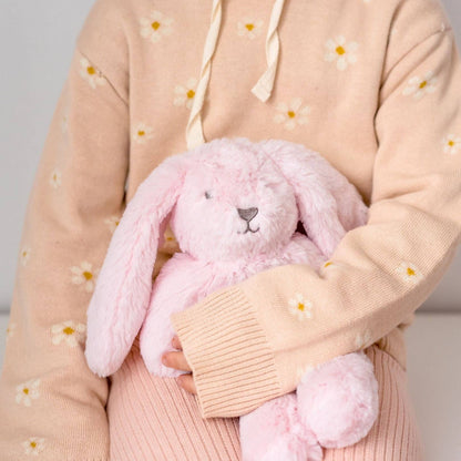 Person wearing a light pink sweater holding a pink plush bunny toy against a neutral background
