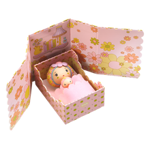 A miniature doll set called 'Rose Tiny Room' with a pink-colored box that opens to reveal a small pink doll and accessories like a bed and a felt cover.