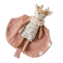 A soft toy depicting a bedtime baby fawn with a floral dress and a leaf-shaped blanket on a pink background.