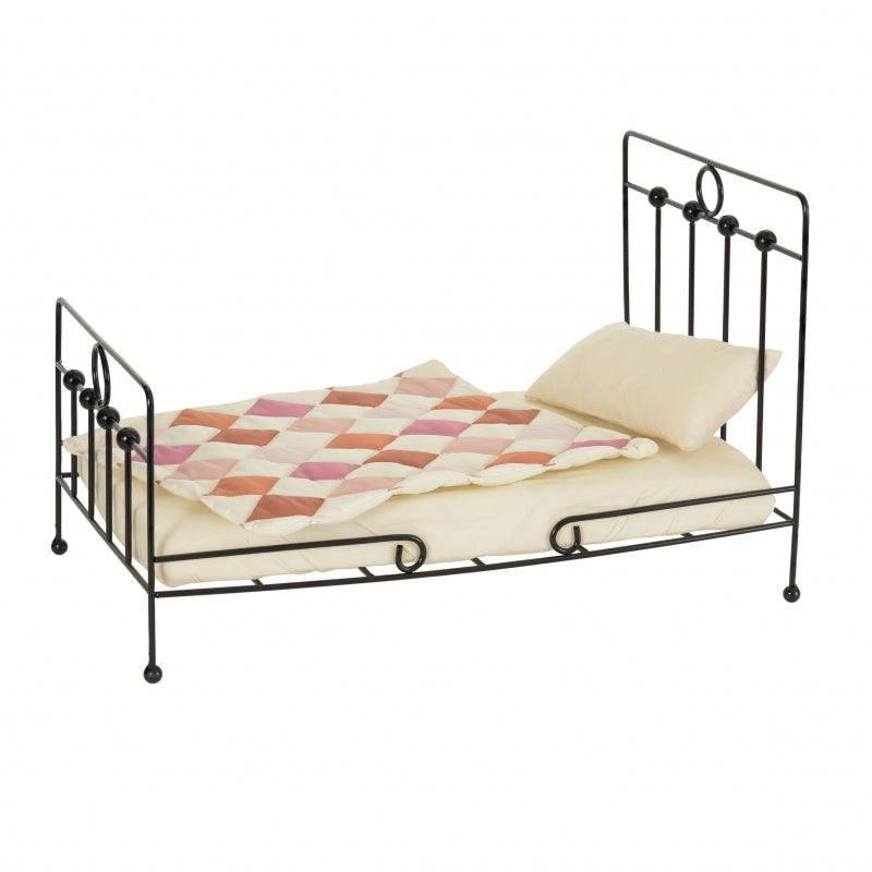 A traditional-style iron doll bed with patchwork quilt, pillow, and mattress.