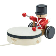A wooden pull-along toy featuring a planer in a red uniform and black hat, marching towards a drum with red drumsticks in hand.
