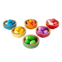 A set of colorful wooden eggs in various shades of the rainbow, placed in matching colored wooden bowls which are stackable.