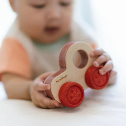 Infant playing with natural wood vehicle toy with large red wheels 