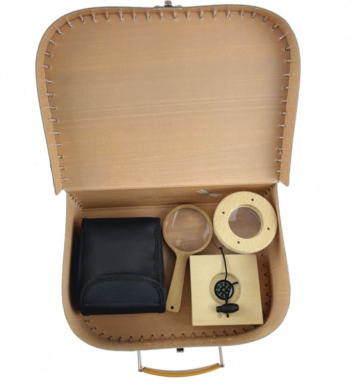 Open brown cardboard case with black pouch, wooden magnifier, and circular object on a white background