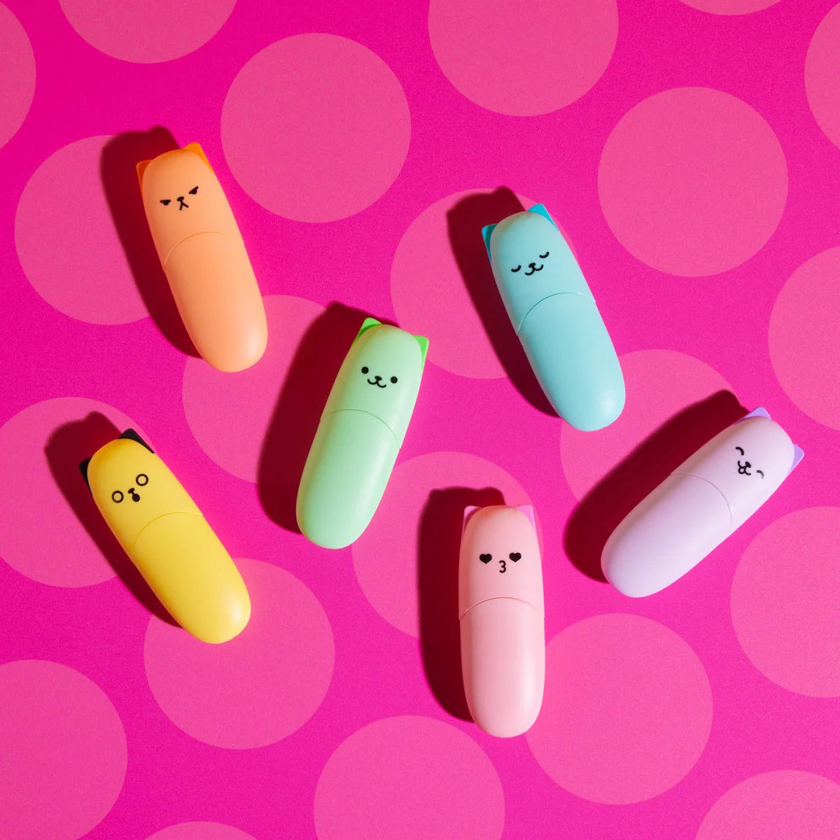 Colorful highlighter markers with cartoon kitten faces on a pink polka dot background