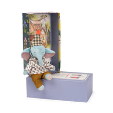 A plush toy elephant doll named Pablo, dressed in a shirt and trousers, sitting on a platform with a illustrated gift box in the background.