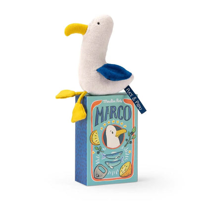 Seagull soft toy with yellow beak and blue wings sitting on an illustrated box with Moulin Roty written on it. 