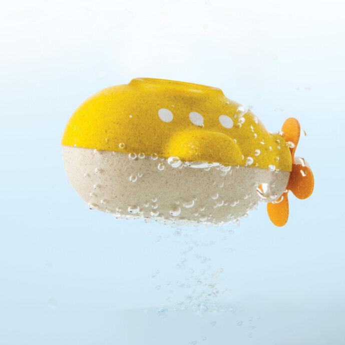 Yellow wooden submarine bath toy with orange rubber propeller, floating in water with bubbles. Plantoy brand