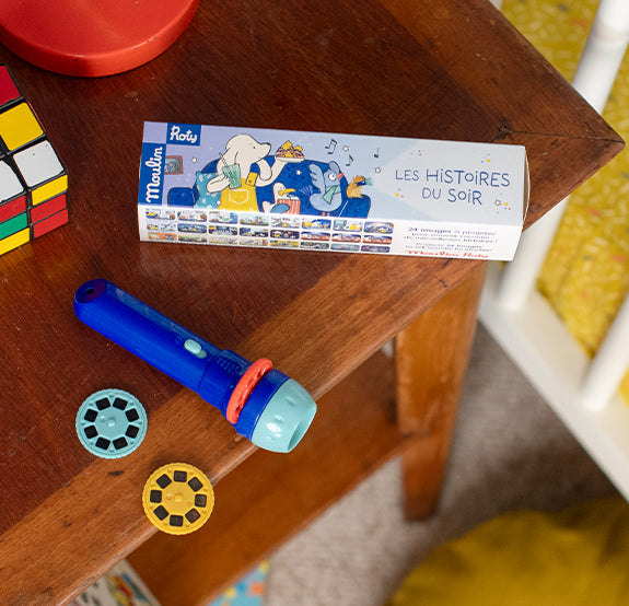 A small blue and red flashlight with plastic discs is displayed on a wooden table alongside a storybook with colorful illustrations.