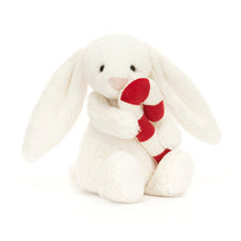 A plush toy depicting a Bashful Bunny with a candy cane. The bunny has cream and scarlet striped fur, cuddly paws, a fluffy tail, and long, floppy ears.